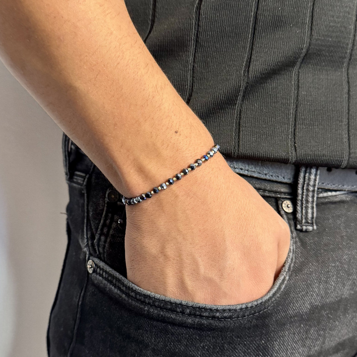 Brățara ZERAH din hematit iridescent și aur 14k purtată pe încheietura unui bărbat, cu mâna în buzunarul blugilor #Culoare_hematit iridescent