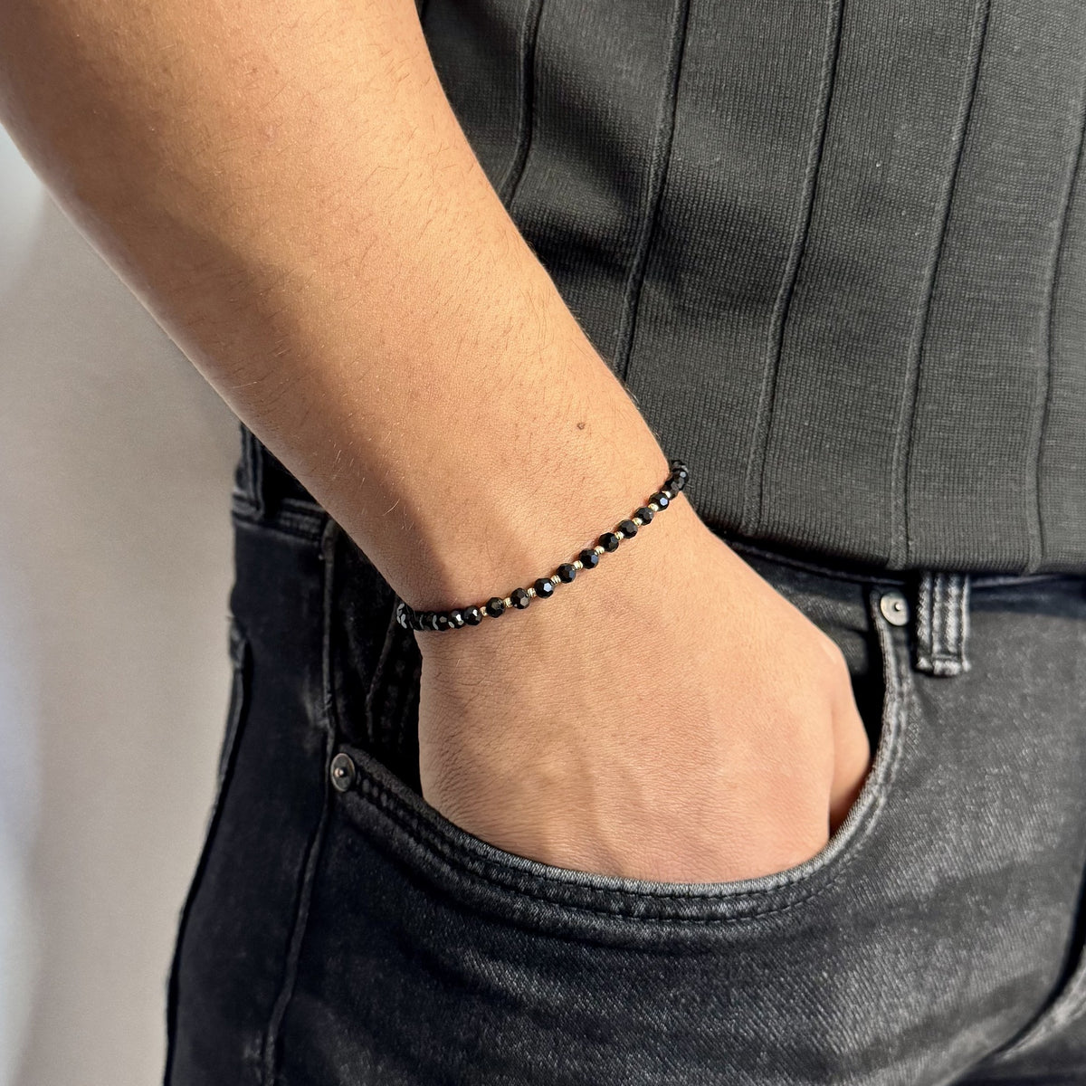 Brățara ZERAH din onix negru și aur 14k purtată pe încheietura unui bărbat, cu mâna în buzunarul blugilor #Culoare_onix negru