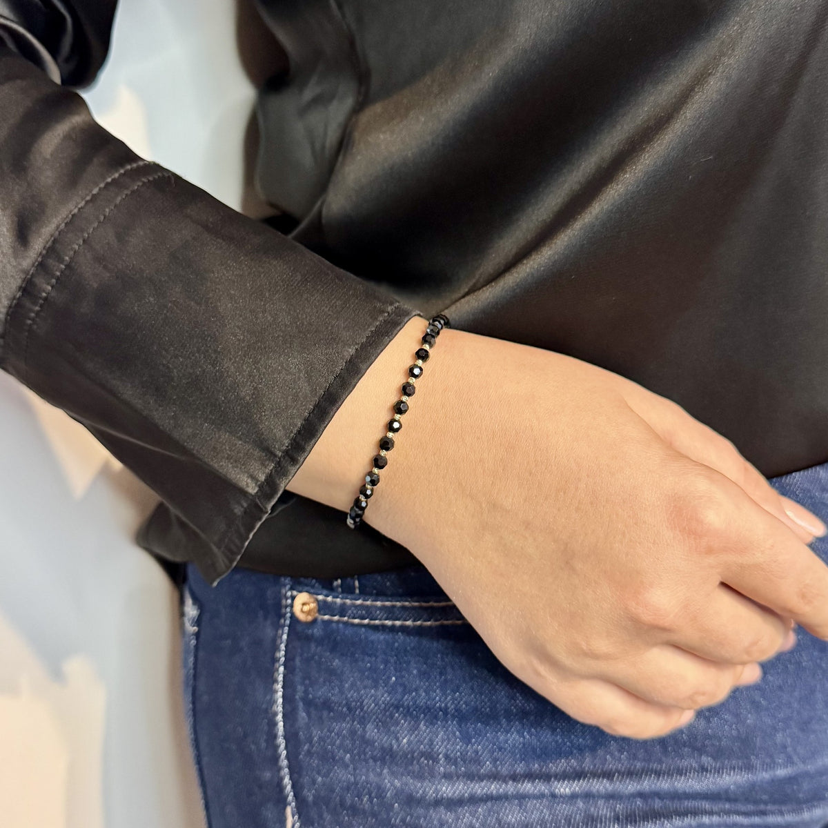 Brățara ZERAH din onix negru și aur 14k purtată pe încheietura unei femei, lângă mâneca unei bluze negre din satin #Culoare_onix negru
