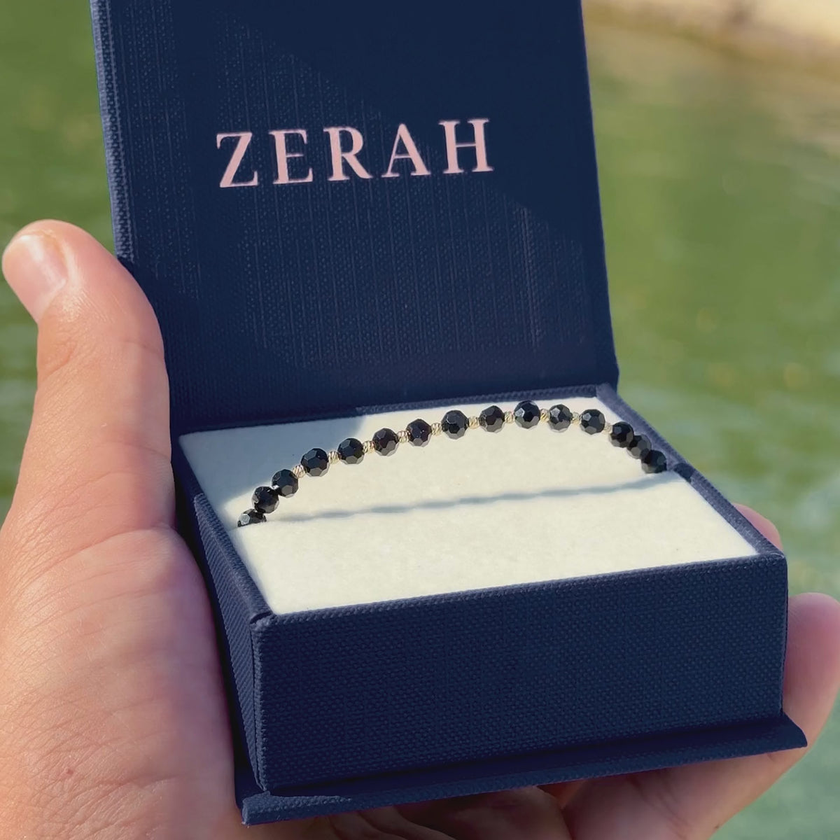 Brățară ZERAH din onix negru și aur 14k în cutia cadou ZERAH, ținută în mână, în lumina soarelui #Culoare_onix negru